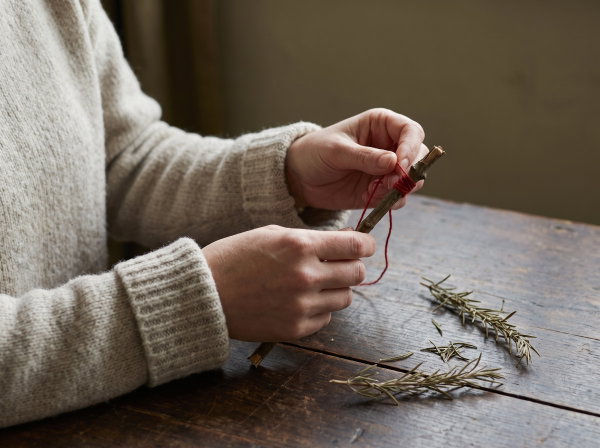 Hands winding red thread around a short rowan twig on a wooden table