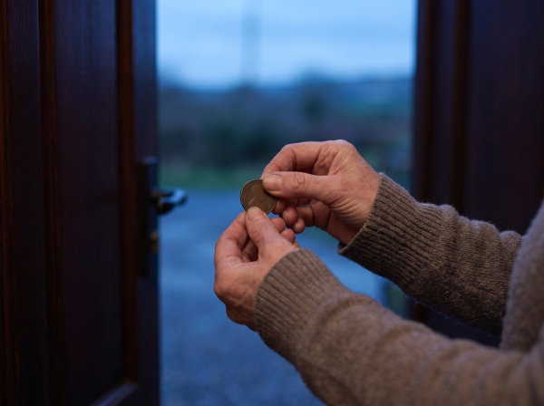 Hands turning a coin over at an open door at dusk
